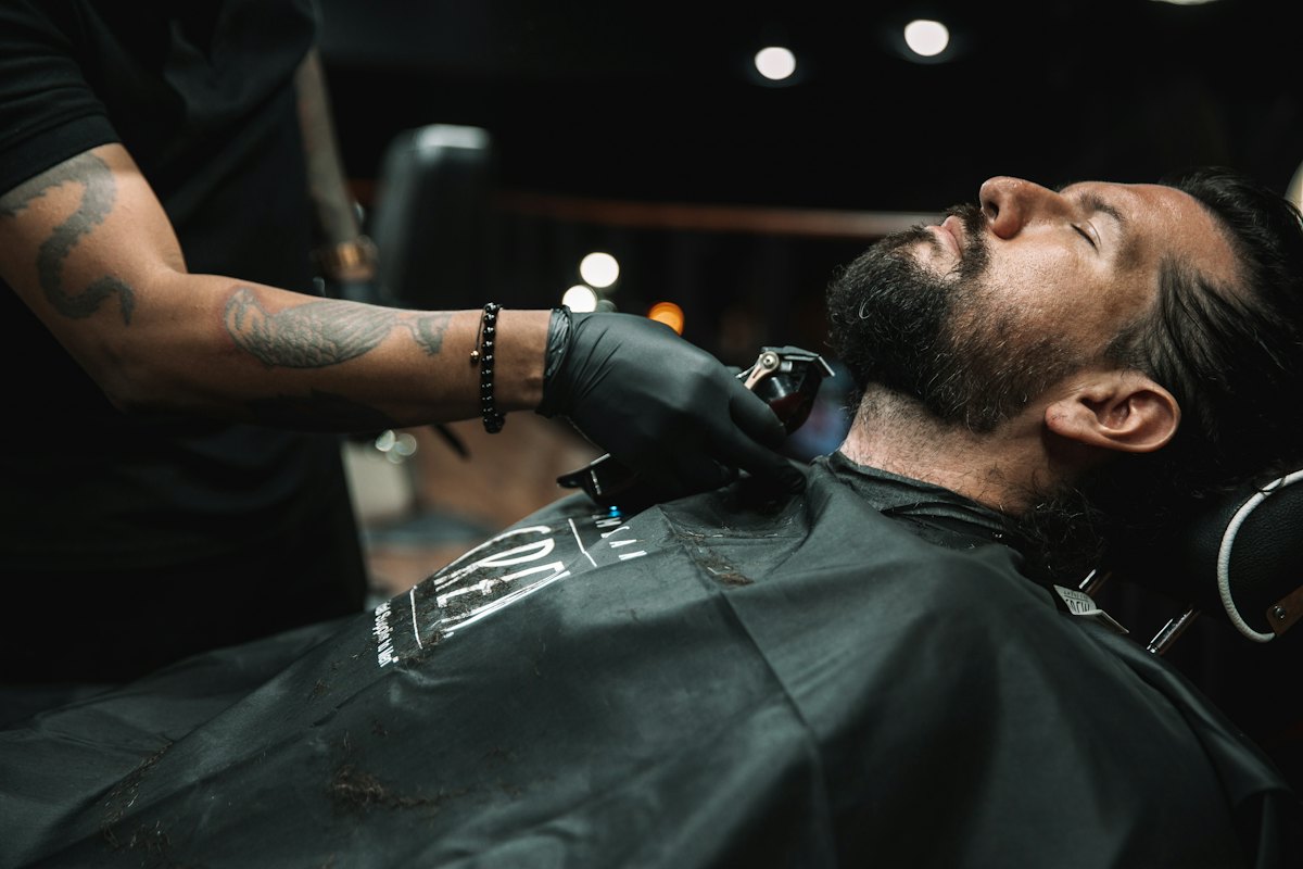 A barber in gloves lining up a customer's beard